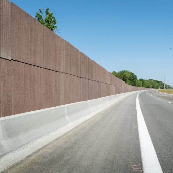 Lange bruine betonnen geluidswand langs een autosnelweg