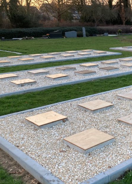 Grafvelden met betonnen afdekplaten en groene zones op een begraafplaats